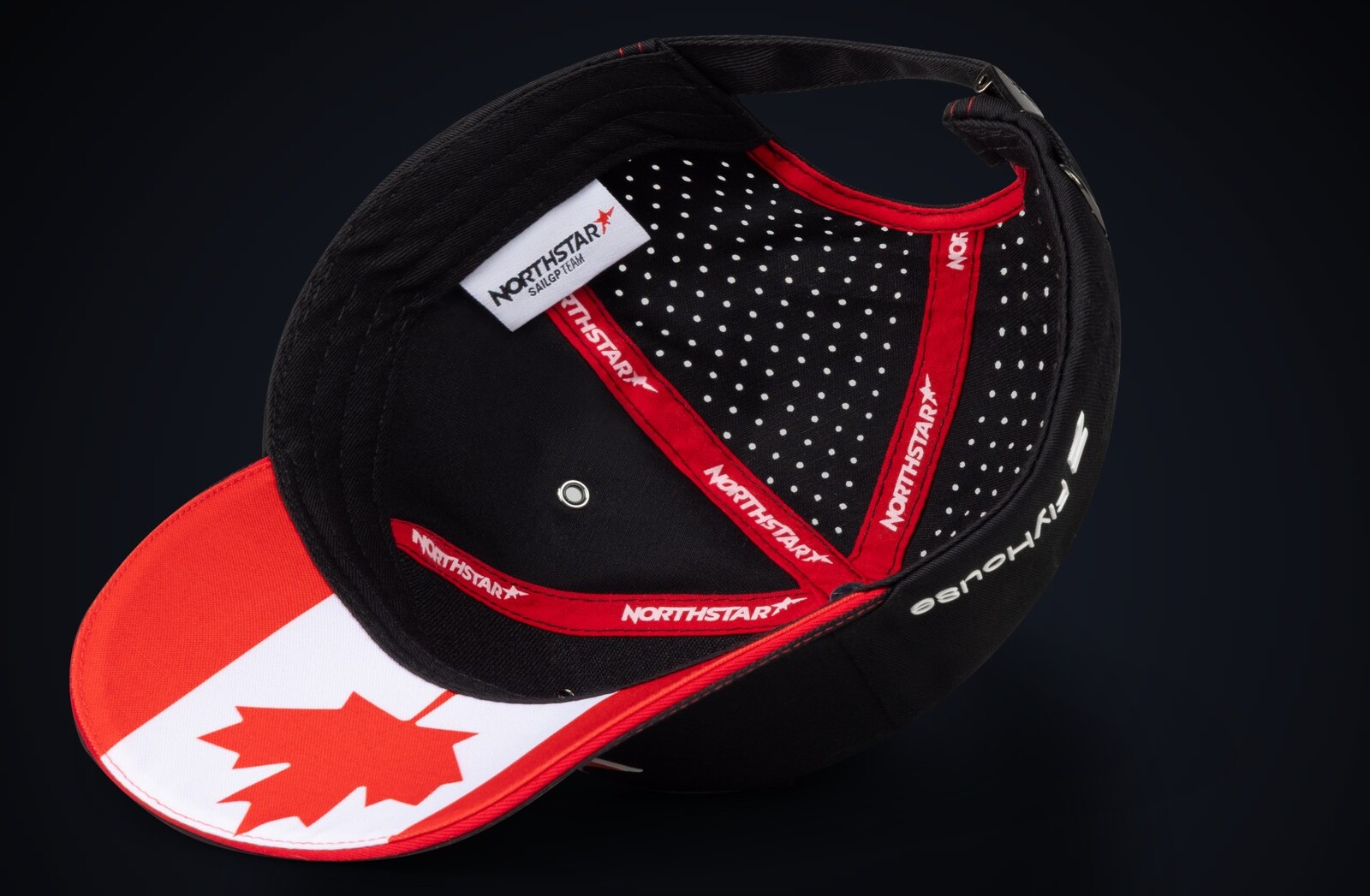 Underside of a bespoke Canada trucker cap showing branded NorthStar seam tape, perforated crown and the maple-leaf flag brim, on a dark studio ground