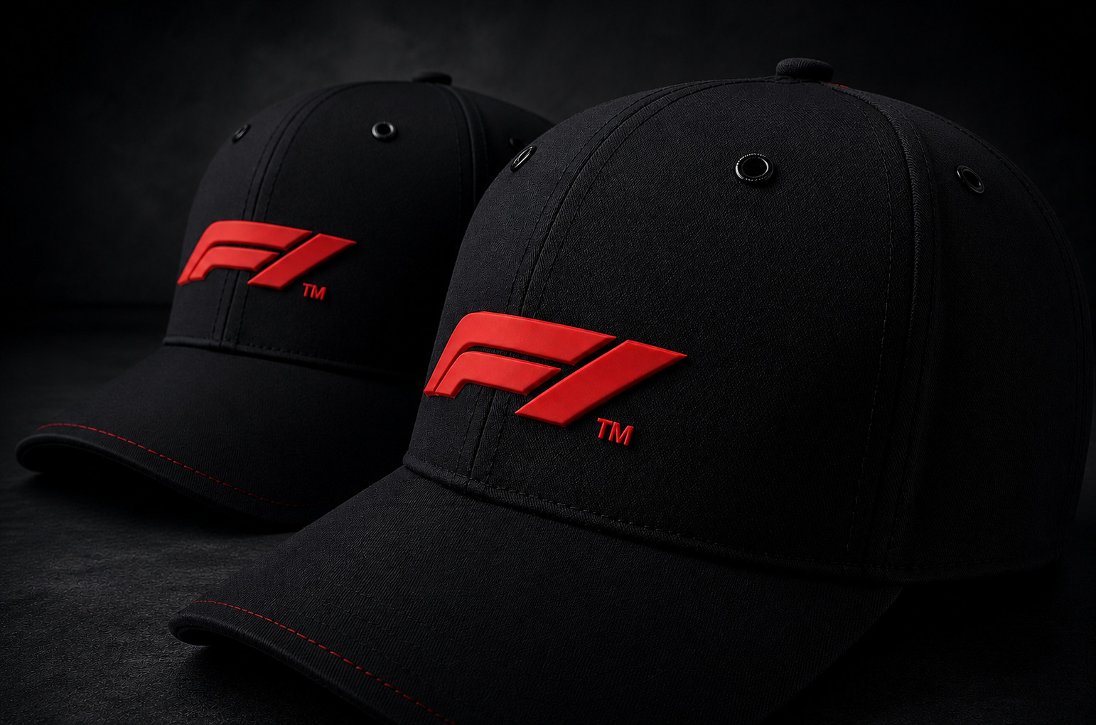 Two bespoke black F1 caps side by side, each with the raised red F1 mark, lit against a dark studio ground