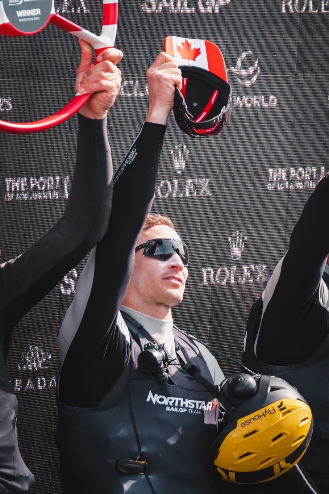 A SailGP athlete lifting a trophy, wearing a branded cap